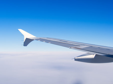 View of aircraft wing against blue sky, flying over a sea of cloudsの写真素材