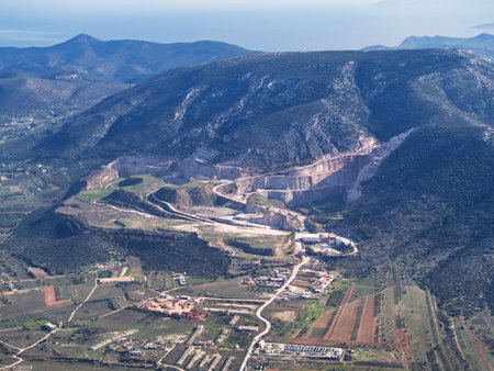Large-scale mining operation nestled in rugged terrain with surrounding mountains and rural areas. Mesogeia, Attiki, Greeceの写真素材