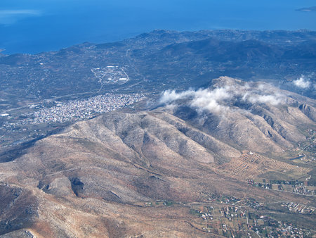 Aerial landscape of mountainous terrain with urban development near coastline and scattered clouds. Ymittos, Attica, Greeceの写真素材