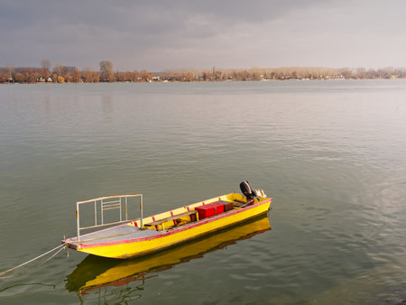 A bright yellow boat floats on a serene river, with autumn trees lining the distant shore.の写真素材