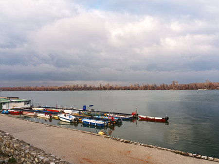 Small boats moored at a Danube riverside dock with cloudy sky and autumn trees in the background. Zemun, Belgradeの写真素材