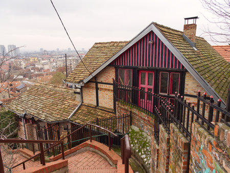 Charming rustic house with red trim perched on hill above city skyline, surrounded by steps and railing in Zemun, Belgrade.の写真素材