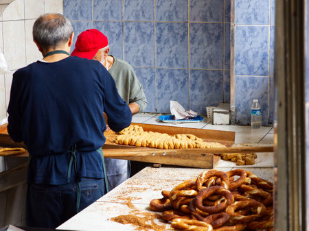 Two people working in a bakery kitchen, shaping pretzels on a wooden table with finished pretzels nearbyの写真素材