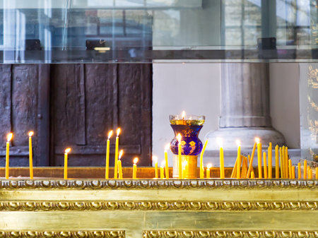 Multiple yellow candles burning on a decorative golden altar with a blue and gold chalice in the centerの写真素材