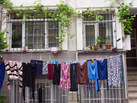 Colorful laundry hanging to dry outside a white building with vine-covered windows and potted plantsの写真素材