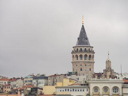 Iconic Galata Tower rising above Istanbul's skyline with colorful buildings and cloudy skyの写真素材