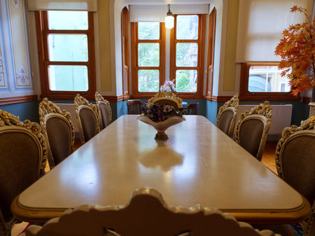 Formal dining room with ornate chairs, long white table, and arched windows with autumn decorの写真素材