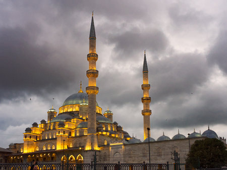 A grand mosque with illuminated minarets and domes against a dramatic cloudy sky at dusk.の写真素材