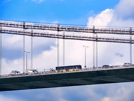 Vehicles crossing a bridge with overhead gantries against a blue sky with white cloudsの写真素材
