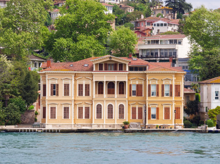 Historic yellow Ottoman-style mansion along the Bosphorus strait in Istanbul, surrounded by lush greeneryの写真素材