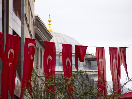 Red Turkish flags with crescent and star hanging in front of a mosque with a white dome and golden spireの写真素材