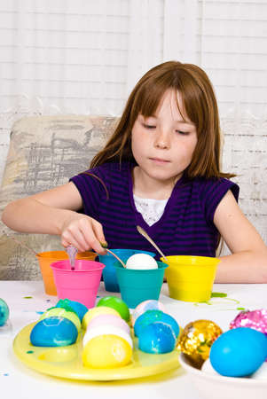 Young girl in the process of coloring Easter Eggs - Step five, the egg half way submerged in the cup of dyeの写真素材