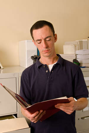 A Caucasian male office worker in a file room reading papers inside a folder.の写真素材