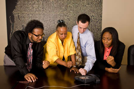 A group of workers stand at a a conference room table during a conference call. All four team members make a fist toward the phone as though someone on the other end made them angry.の写真素材