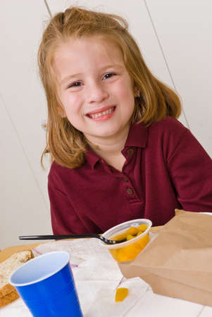 Young school girl smiling while eating lunchの写真素材