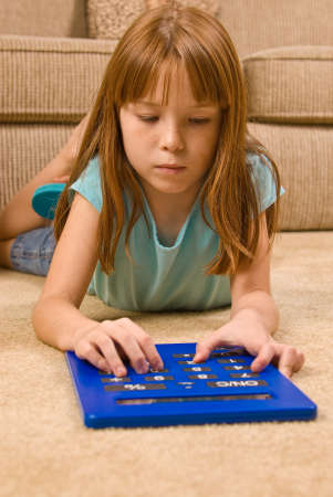 A young red headed female child lays on the floor and works on an oversized calculator.の写真素材