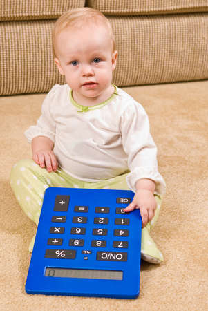 A young baby in a pair of generic PJs sitting on a living room floor with a large oversized calculator.の写真素材