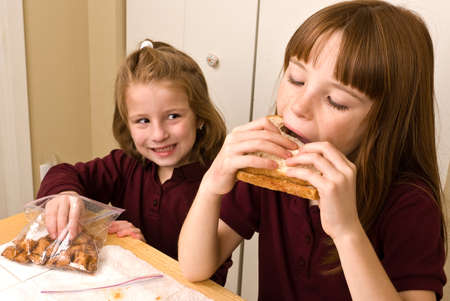 Young school girl eating lunch while another sneaks a pretzelの写真素材
