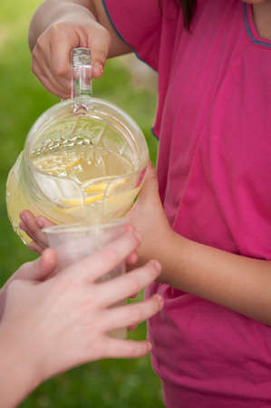 A young girl pouring lemonade from a glass pitcher into a plastic cupの写真素材