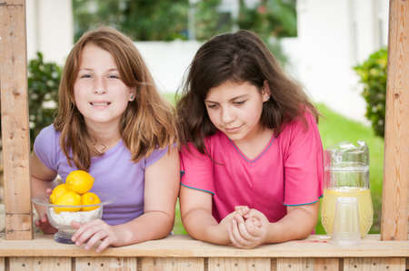 Two bored young girls at their lemonade stand with no customersの写真素材