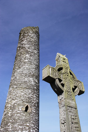 Irish Cross in front of a Monastic round tower and blue skyの写真素材