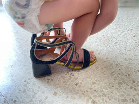 Baby in diapers buckling her shoes in women's high heelsの写真素材