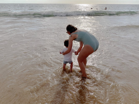 View from behind a happy woman bathing with a child on the beachの写真素材