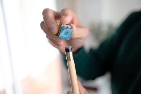 A billiard player prepares to play by putting blue chalk on his cue. Details of the game of...