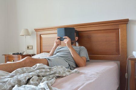 Young man relaxing sitting on his bed reading an ebook on the weekendの写真素材