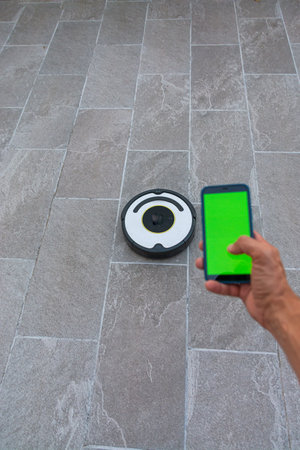 Smartphone with green screen and robotic vacuum cleaner on the floor.の写真素材