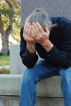 Man sitting at gravesite with his head in his handsの写真素材