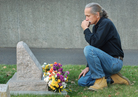 Man sitting at gravesite with a look of sadnessの写真素材