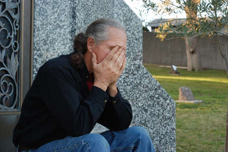 Man sitting at gravesite with his head in his handsの写真素材