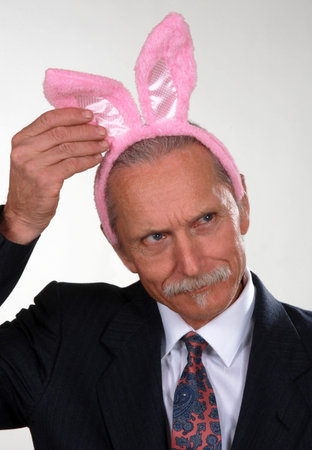 Middle aged man wearing pink bunny ears, touching the ears, looking curious and confused