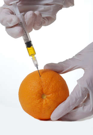 Close up of hands injecting fluid into an orange.の写真素材