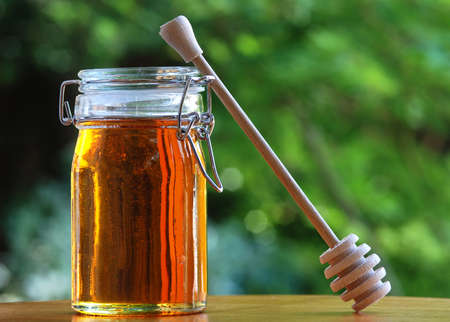 A jar of honey with stir stick, natural outdoor backgroundの写真素材