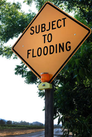 Yellow warning sign on the side of a rural lane: 'Subject to Flooding'の写真素材
