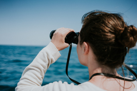 A woman looking through binoculars on the ocean.の写真素材