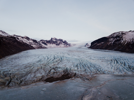 A glacier in Iceland between some mountains with a frozen lake in front of itの写真素材