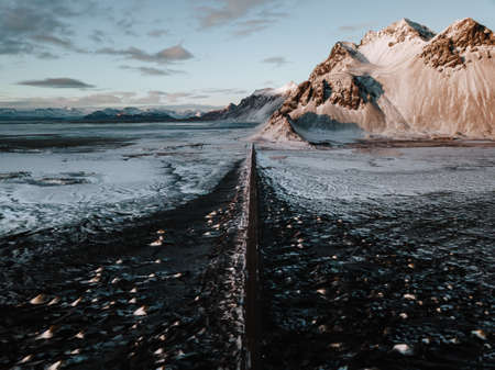A road leading towards a mountain through a snow covered landscape in Stokksnes, Iceland. The photo is taken using a drone.の写真素材