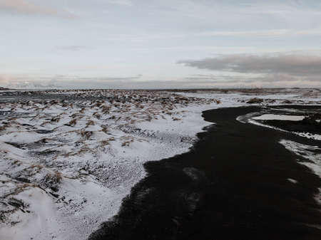 A drone capture of a black sand beach at Stokksnes, Iceland next to a snow covered field.の写真素材