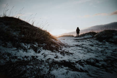 A person walking over a black sand beach, partly covered in snow at sunset at Stokksnes, Iceland.の写真素材