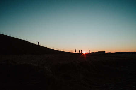 Silhouettes of people walking up a hill at sunrise in Iceland close to the famous waterfall Skogafossの写真素材