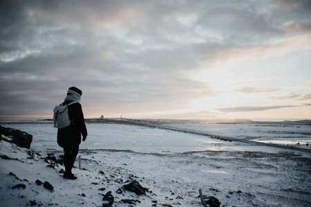A person standing on top of a hill, looking over the snow covered landscapes of Stokksnes, Iceland at sunset.の写真素材
