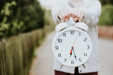 A woman holding a clock in front of her into the cameraの写真素材