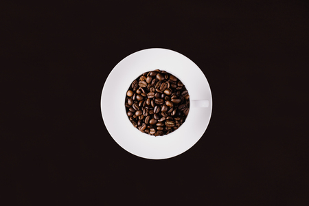 A mug filled with coffee beans and a plate underneath on a dark backgroundの写真素材