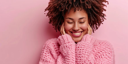Self-care concept. Portrait of a beautiful happy woman hugging herself with confidence, savoring her cozy new blush pullover, tilting her head and standing indoors.の素材