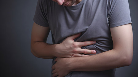 Close-up of a man experiencing liver pain against a gray backdrop.の素材