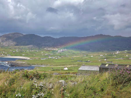 Irish country village with rainbow and dark mountainsの写真素材