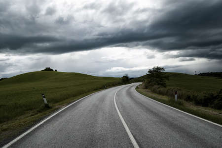 Road between fields under a cloudly skyの写真素材